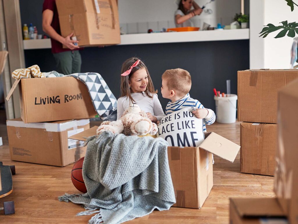 Two young children playing in a box on moving day in their new freehold family property