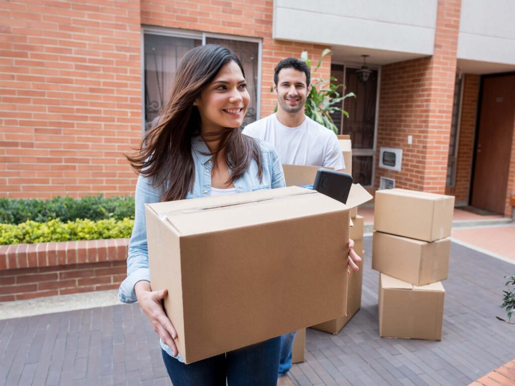 A young woman and man carrying boxes into their new build home after a purchase made using ONP Solicitor's legal services