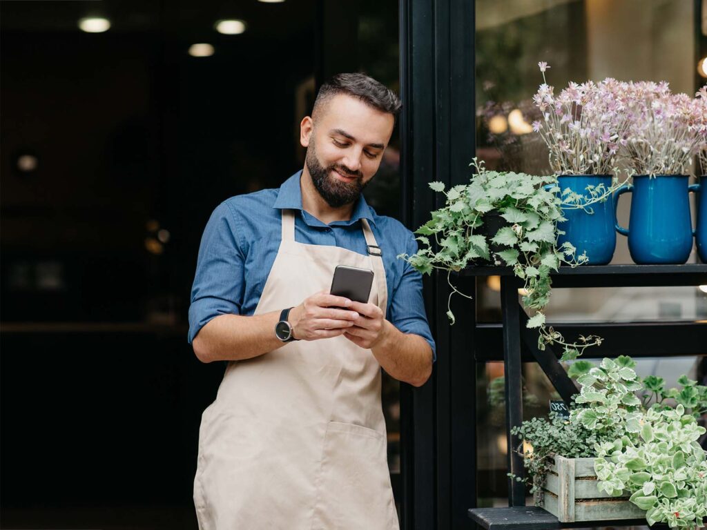 A young business owner stood in the doorway of his shop on his mobile app using ONP Solicitor's commercial legal services