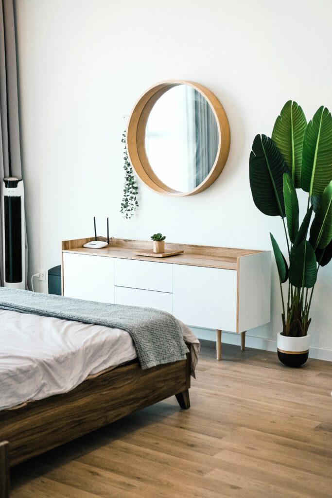 An image of a bedroom, showing a dresser and a modern mirror, with a houseplant